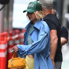 Gigi Hadid wearing a blue trench coat, butter yellow trousers, Birkenstocks, and a yellow Miu Miu bag in New York City July 2024