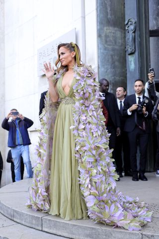 Jennifer Lopez walking into a fashion show wearing a long green gown and a floral cape by elie saab