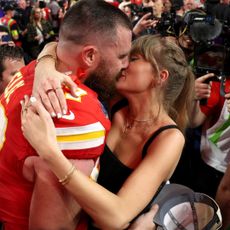 a close up photo of Taylor Swift and Travis Kelce kissing at the Super Bowl while taylor swift waring a black corset