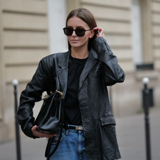 Diane Batoukina wears sunglasses, a black top, a black leather oversized blazer jacket, a Hermes belt, blue denim wide-leg flared jeans / pants, a Hermes bag, during a street style fashion photo session, on March 17, 2023 in Paris, France. 