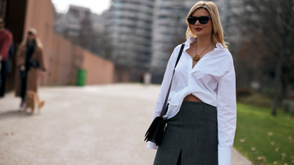 A guest attends the milan fashion week spring summer 2024 in a white button down, grey skirt, black sunglasses, and crossbody bag