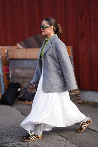 COPENHAGEN, DENMARK - FEBRUARY 01: A guest wears green sunglasses from Loewe, a green shirt, a gray oversized blazer jacket , a white gathered midi dress, brown leopard print pattern Adidas sneakers shoes , a black fluffy bag, outside Gestuz, during the Copenhagen Fashion Week AW24 on February 01, 2024 in Copenhagen, Denmark. (Photo by Edward Berthelot/Getty Images)