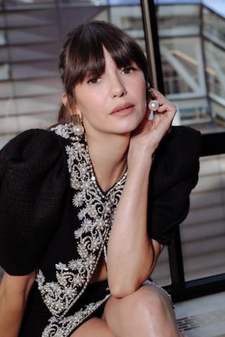 Nina Dobrev sits in front of the camera wearing pearl earrings and a beaded matching set by Carolina Herrera