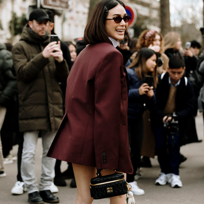 a guest attends the Paris fall 2024 fashion week shows wearing oversized dark red blazer, sunglasses, and black miu miu bag 