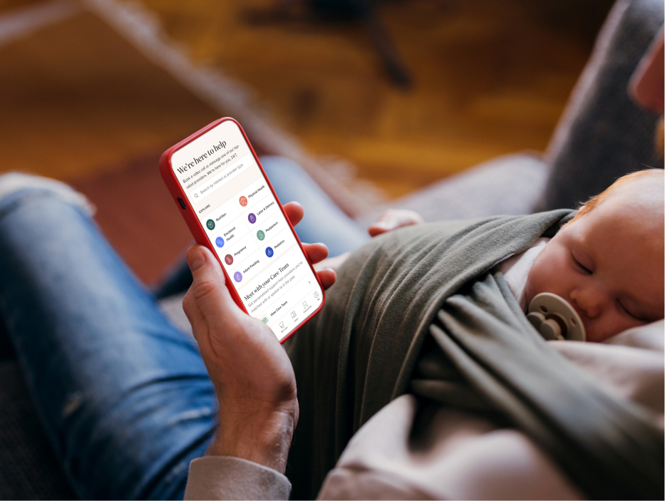 A person with a sleeping baby on their chest, holding a phone with the Maven Clinic app open