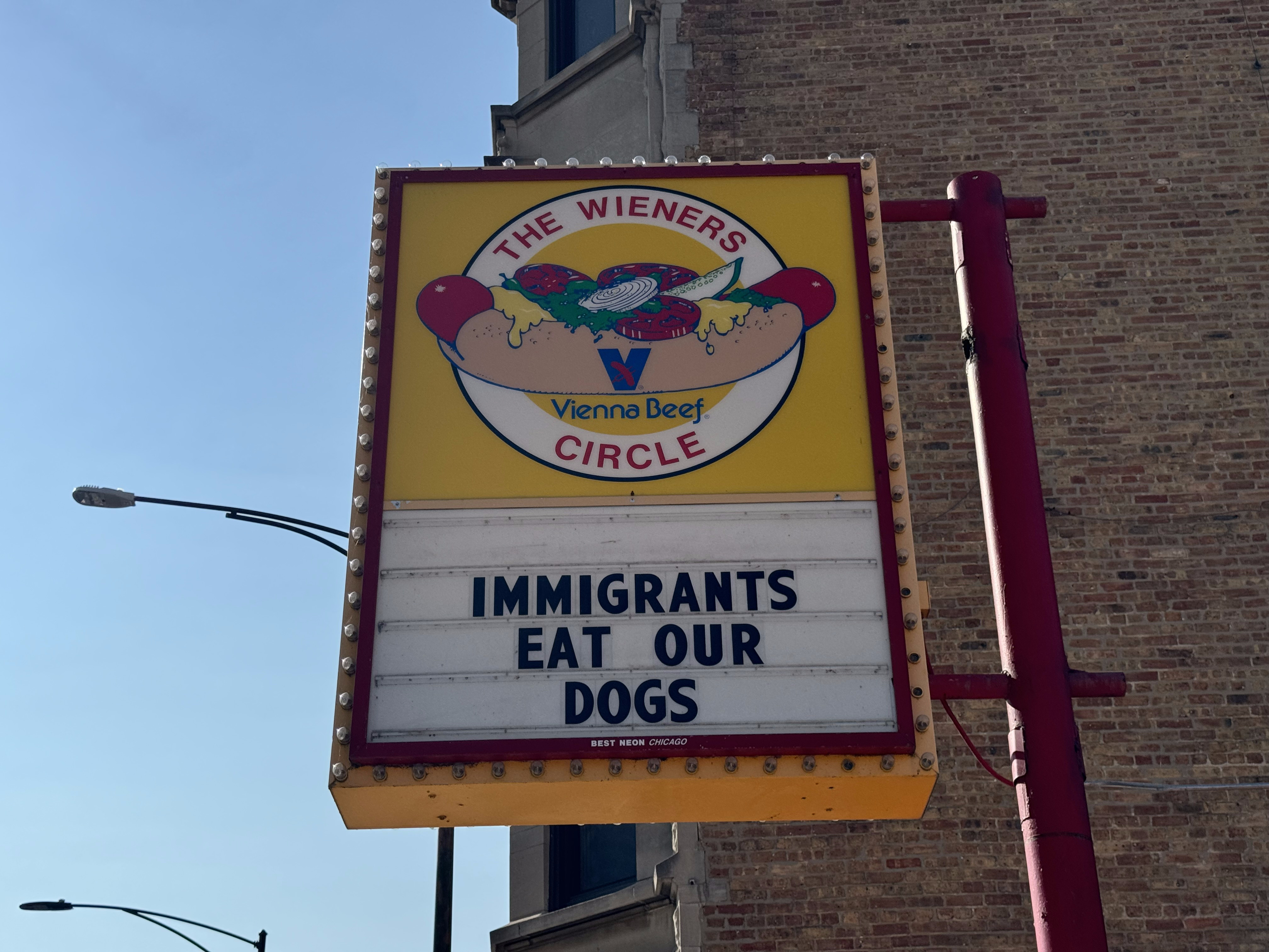 Wieners Circle’s sign in sunlight reading “Immigrants Eat Our Dogs”