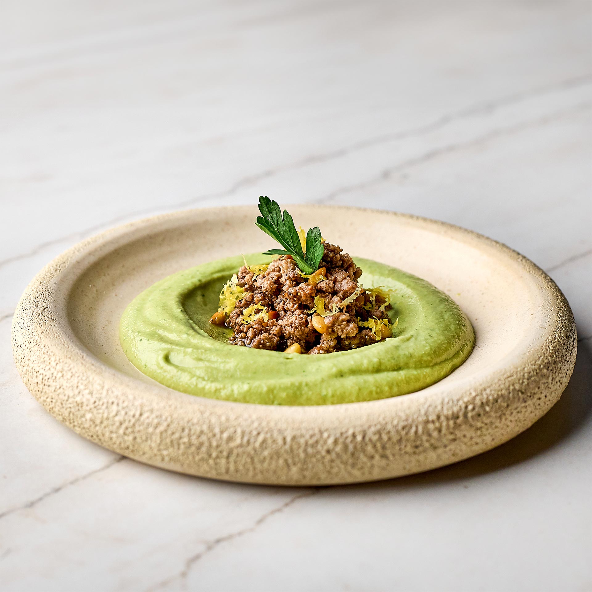 A circular dish with green hummus with herbs.