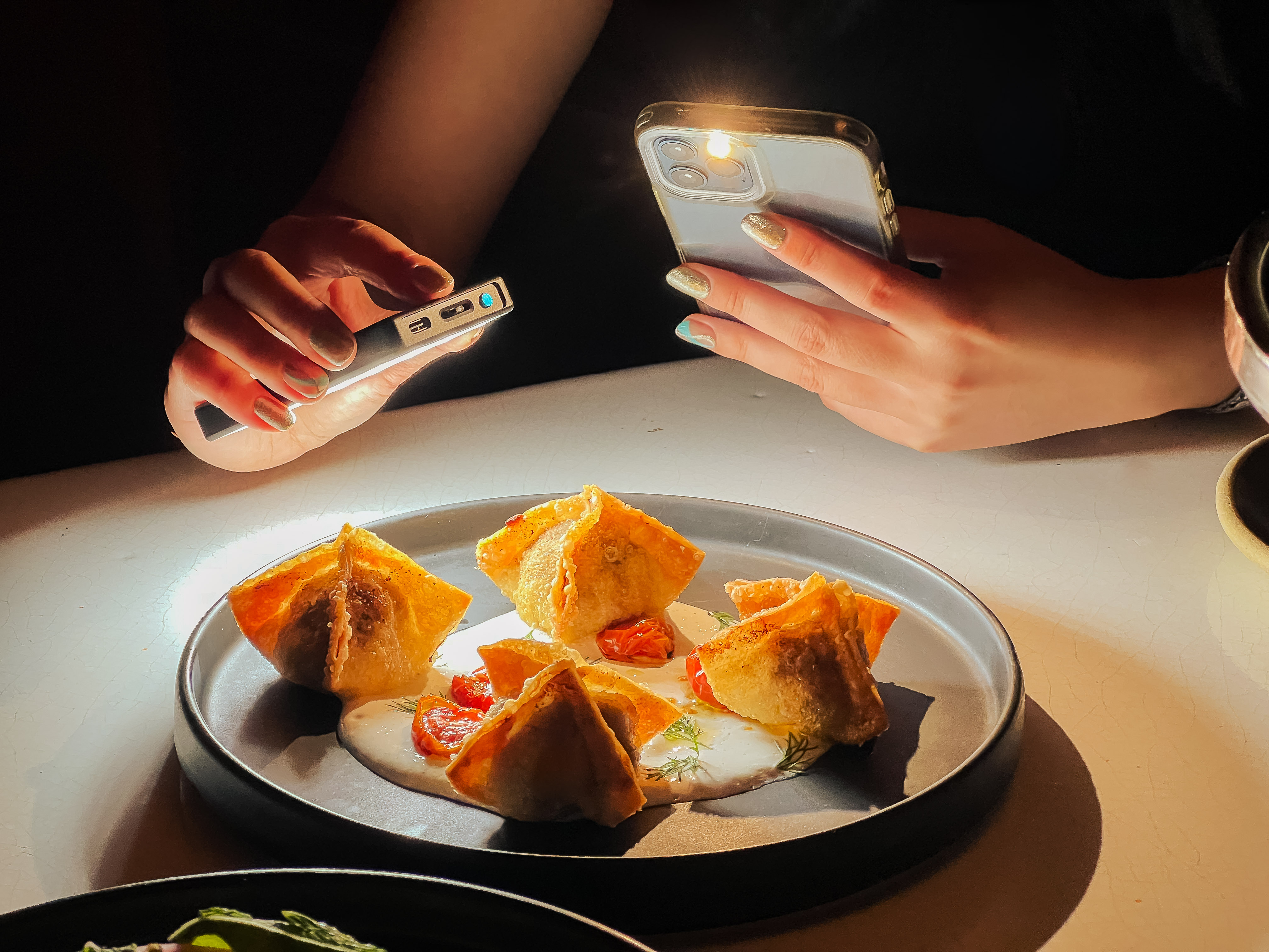 A person holds a light in one hand and a phone in another as they photograph a plate of fried manti.