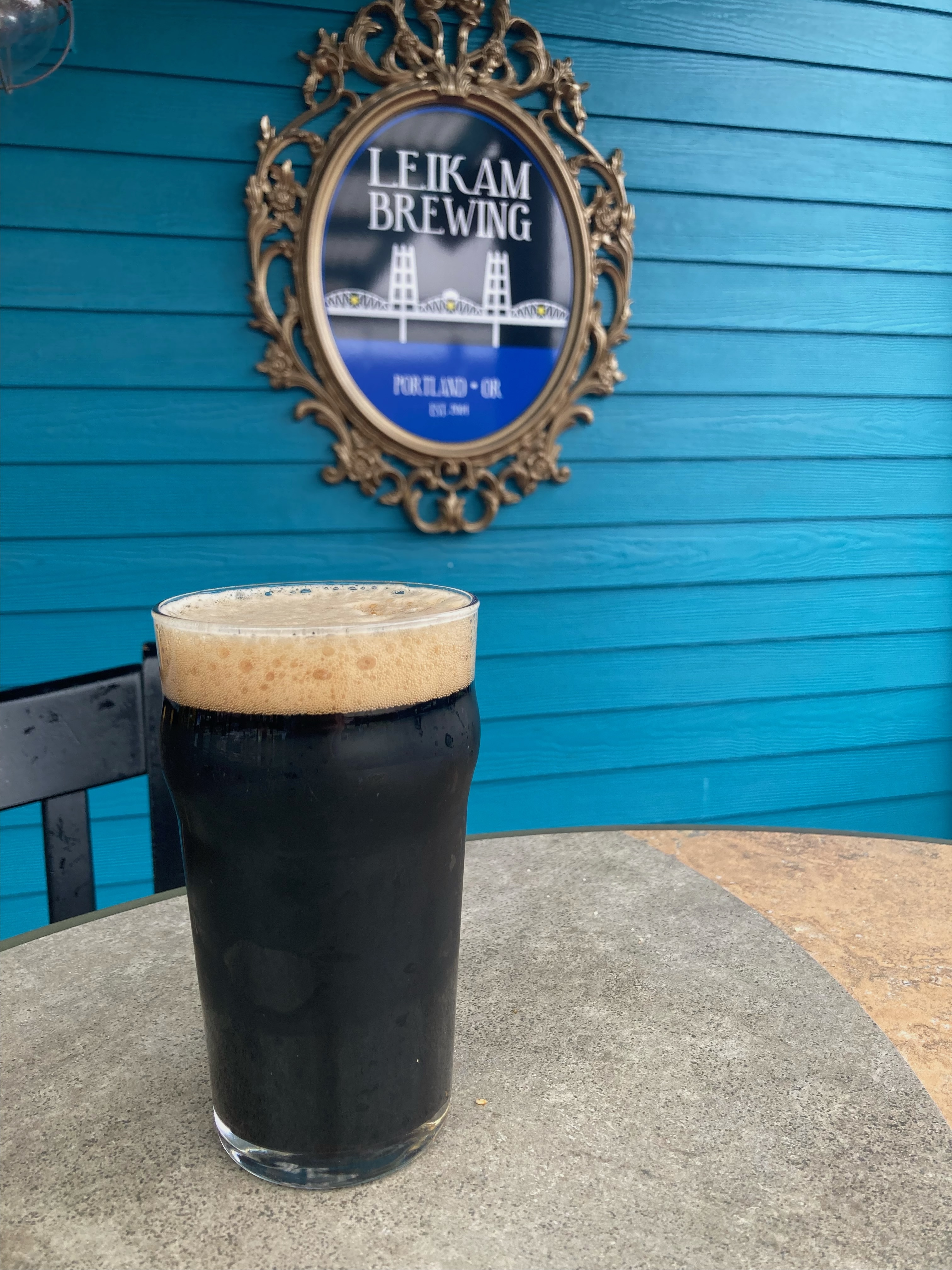 Glass of dark stout beer in front of a blue wall that says Leikam Brewing