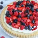 Fruit tart topped with red and blue berries on a white plate.