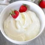 Whipped cream in a white bowl with strawberries.