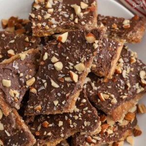 Graham cracker toffee topped with chopped almonds on a white plate next to a red and white striped napkin.