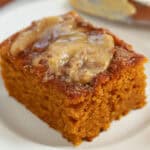 Slice of pumpkin cake topped with honey butter on a white plate.