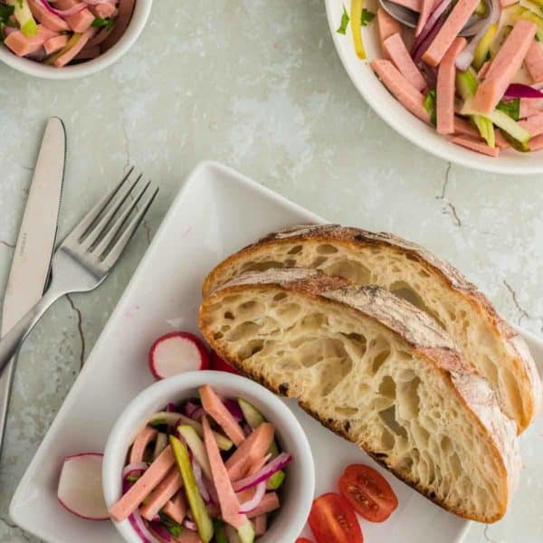 a bowl of Wurstsalat served with hearty bread a side of sliced tomatoes