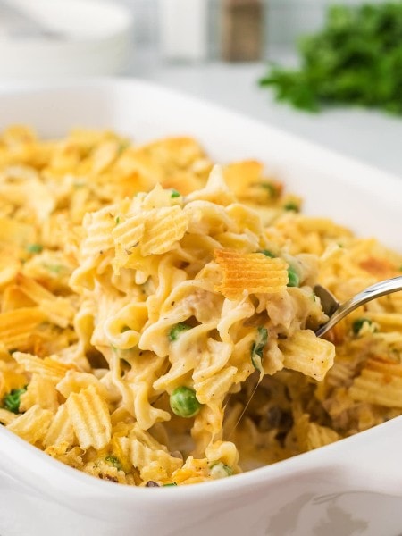 Tuna Casserole being served in a white casserole dish with a serving spoon.