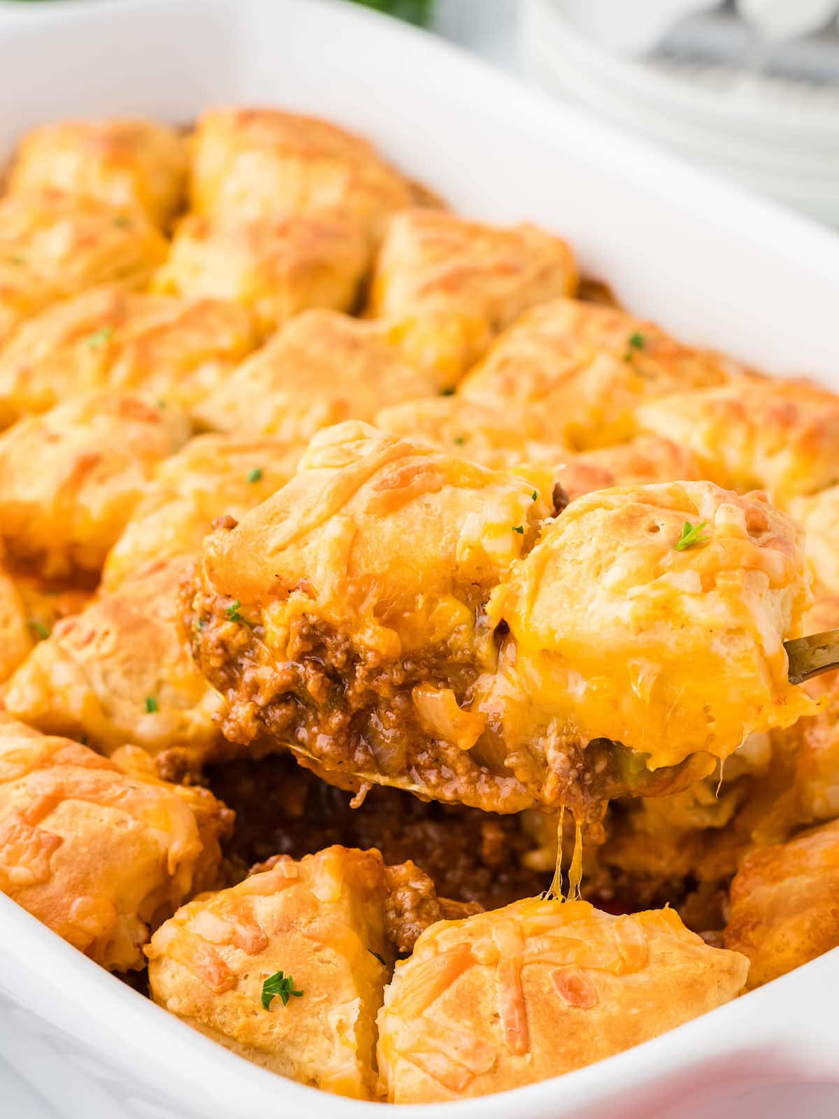 Closeup of a serving spoon full of Sloppy Joe Casserole in a white baking dish.