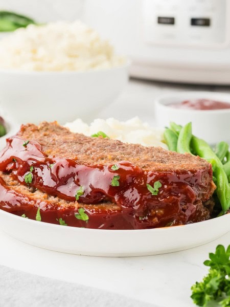 Two slices of Meatloaf made in a Crockpot served on a white plate.