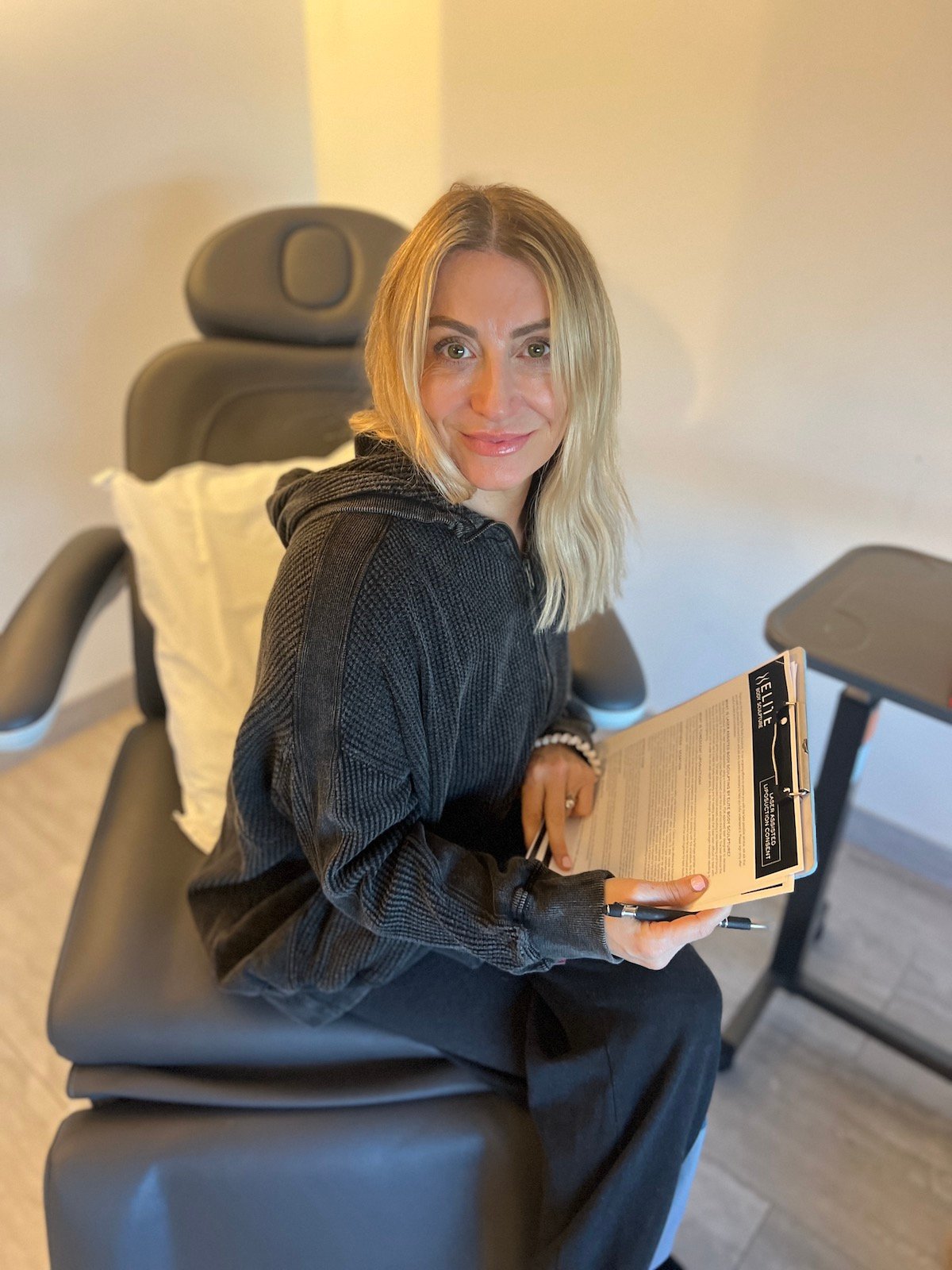 A woman sits on a chair filling out an intake form in a medical office.