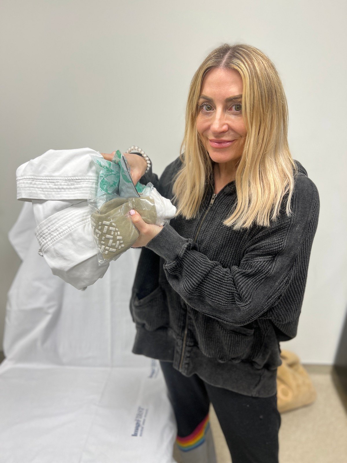 A woman holds up a robe, socks, and facemask in a doctor's office.