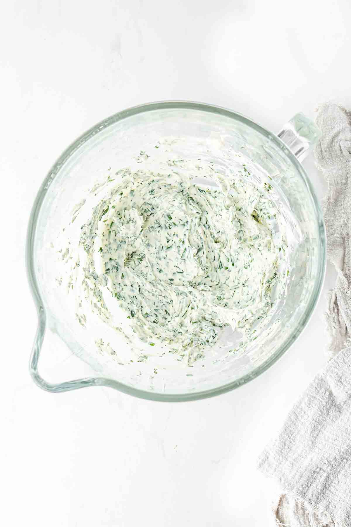 Whipped herbed cream cheese in a large glass mixing bowl.