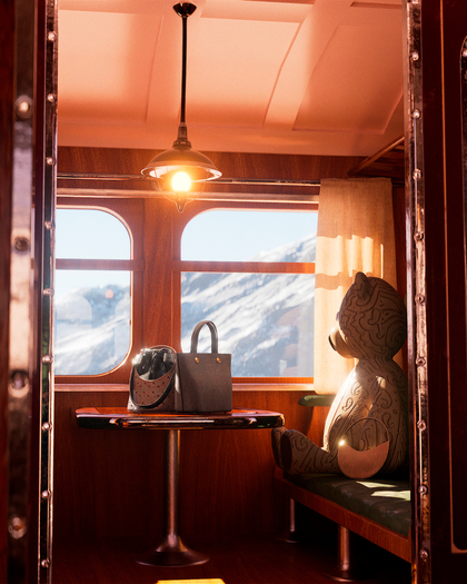 Interior of a vintage train compartment with a large wooden bear sculpture sitting on one side of a small table. The table holds two bags—one black with a bucket shape and another gray with handles. A warm overhead light illuminates the wood-paneled room, casting a cozy glow. Through the windows, a scenic snowy mountain landscape is visible under a bright blue sky.