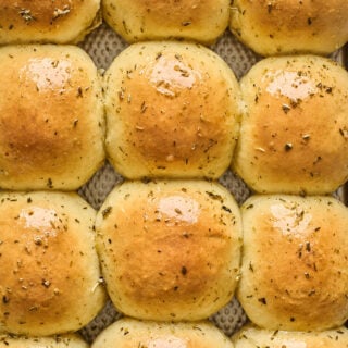 Twelve potato rolls on a baking sheet after being glazed