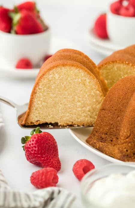 A slice of pound cake being removed to serve with fresh berries and whipped cream