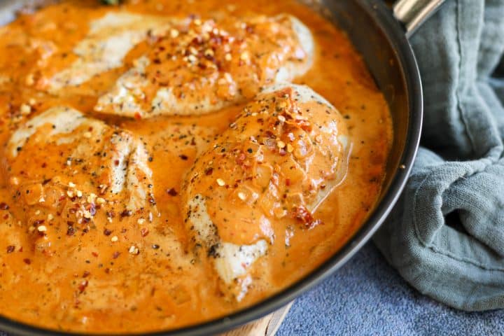 chicken breasts in a pan with pesto sauce.