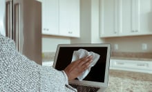 Close-up of unrecognizable woman in kitchen cleaning laptop screen with disinfectant wipe