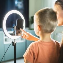 Mother live streaming with son on smart phone with ring light at home.