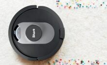 a shark robot vacuum cleans a white carpet