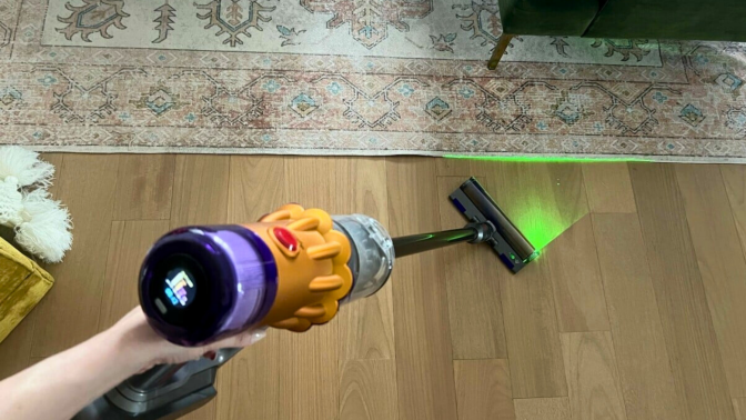 Person holding Dyson V12 Detect Slim to clean hardwood floor with laser on