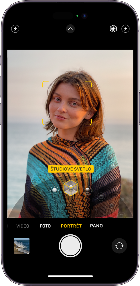 Obrazovka Kamera v režime Portrét. Objekt v hľadáčiku je zaostrený, pozadie naopak rozostrené. V dolnej časti rámčeka je otvorený kruhový ovládač na výber osvetlenia portrétu a na ňom je vybraný efekt Štúdiové svetlo. V ľavom hornom rohu obrazovky je tlačidlo Blesk, v strede hornej časti je tlačidlo Ovládanie kamery a vpravo hore sú tlačidlá na úpravu intenzity osvetlenia portrétu a hĺbky ostrosti. V spodnej časti obrazovky sú sprava doľava nasledovné tlačidlá: tlačidlo prehliadača fotiek a videí, tlačidlo Odfotiť a tlačidlo na výber kamery prepnuté na zadnú kameru