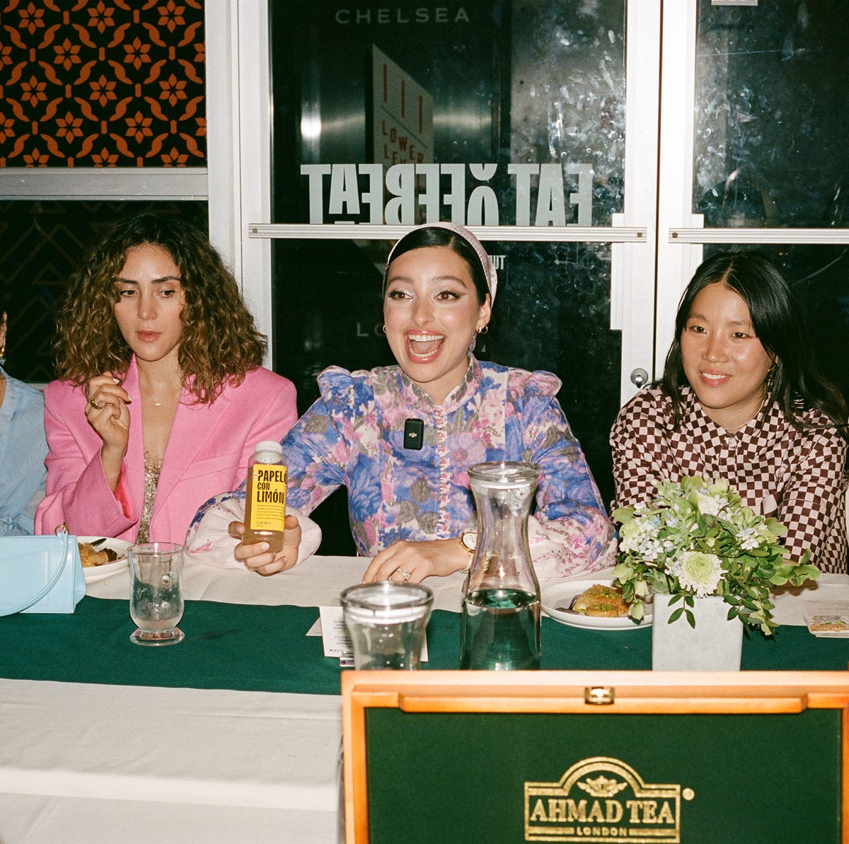 noor, smiling wide, sits in between a group of people at a long table