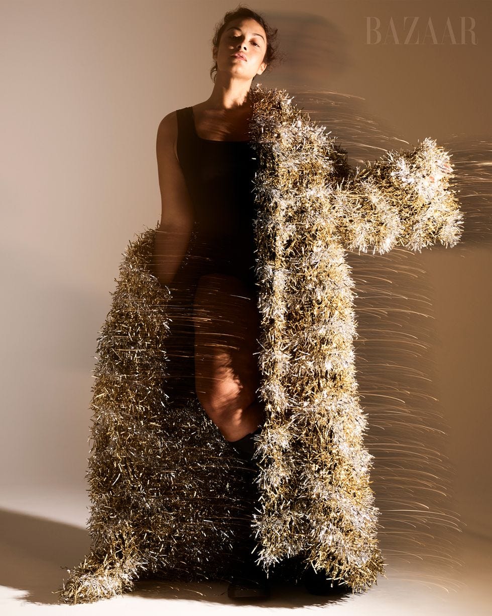 woman standing in gold and white floor length coat over black bodysuit