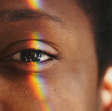 half of a black womans face with a rainbow light reflection over her eye