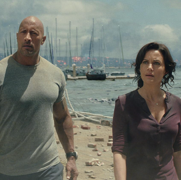 a man and woman standing on a beach with boats in the background