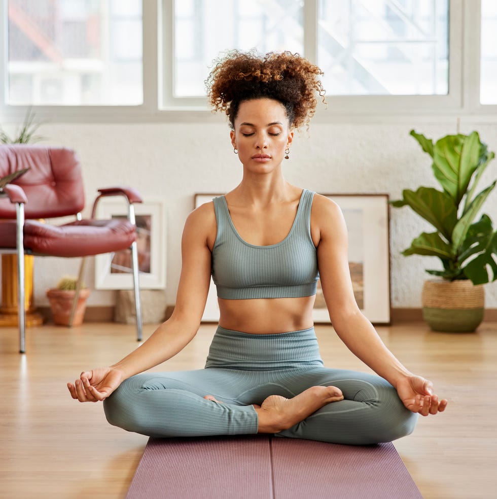 full length of woman practicing breathing exercise young woman with eyes closed sitting in lotus position she is living room at home