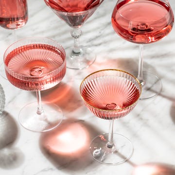 pink rose cocktail or mocktail with sunny summer light on white marble table and palm tree shadows