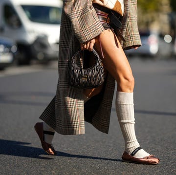 paris, france october 04 caroline daur wears a beige and white checkered print pattern wool polo shirt, brown and burgundy shiny leather shorts from miu miu, a beige with brown dark green red houndstooth print pattern oversized long coat, a brown shiny leather embossed handbag from miu miu, beige ribbed wool high socks, brown satin ballerinas , outside miu miu, during paris fashion week womenswear springsummer 2023, on october 04, 2022 in paris, france photo by edward berthelotgetty images