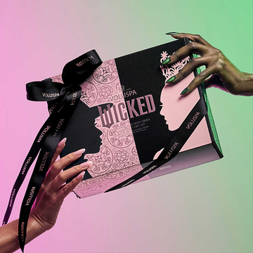 a sequin black shirt beside it a hands holds a gift box from voluspa featuring a pink background and black decorative elements highlighting the word wicked along with intricate designs