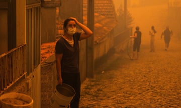 A woman wears a face mask while surrounded by orange smoke amid a forest fire in Portugal