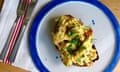 Topview of scrambled eggs studded with bacon, and sprinkled with chopped chives, on a round white plate.