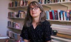 Author Sarah Moss sits on a chair in front of a wall of books on shelves.