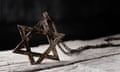 the star of david on a rustic wooden surface<br>closeup of an old and rusty pendant in the shape of the star of david on a white rustic wooden surface, against a dark background