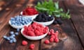 Bowls of raspberries, blueberries and blackberries on a brown picnic table