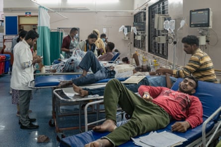 A busy hospital ward with medics attending to male patients lying on gurneys 