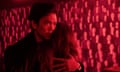 film still of man hugging woman against red-lit background of faces