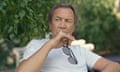 Robert Lindsay sitting in a garden chair, holding his sunglasses and looking thoughtful