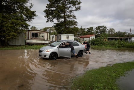 Men push a silver sedan through the flooded streets by a trailer park